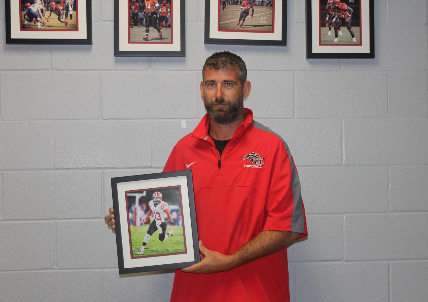Head football coach Alan Peacock holds a framed photo of Dan Ellington, a 2016 CHHS graduate who played quarterback for the Mustangs. Ellington is now quarterback for Georgia State University.