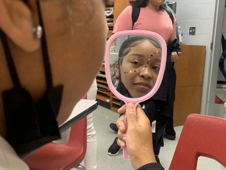 Jada Parker, sophomore, looks at her reflection after Art Society member Carrie Cardin, junior, painted her face with red, white and black dots for Game Day.